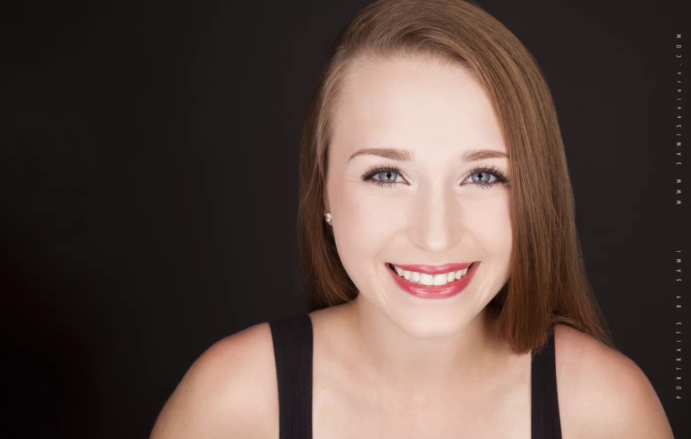 Woman with straight light brown hair and light skin smiling at the camera against a plain dark background, wearing a black sleeveless top—perfect for a classic high school Senior Yearbook picture.